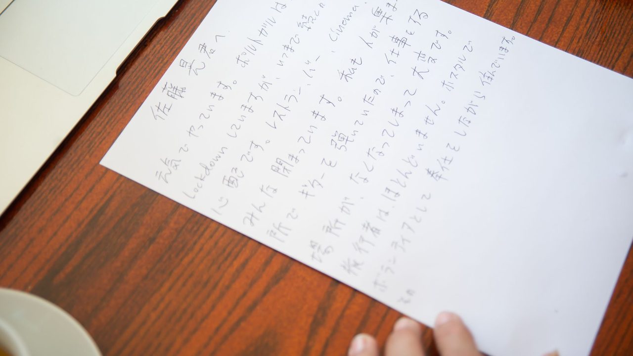 Close-up of a handwritten Japanese letter on a wooden desk with a laptop and tea cup.