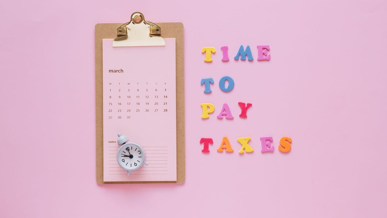 A flat lay of a March calendar and 'Time to Pay Taxes' letters on a pink background.