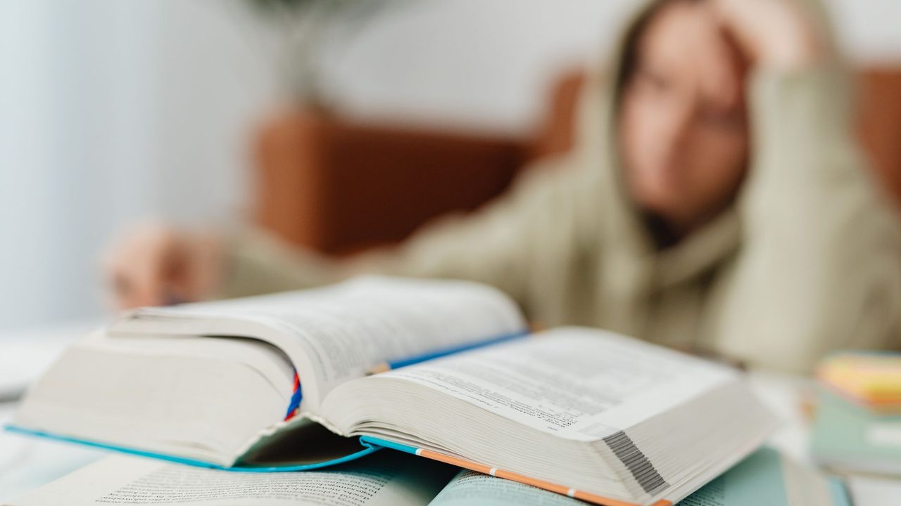 Blurred student studying at desk with open books, showcasing academic stress.
